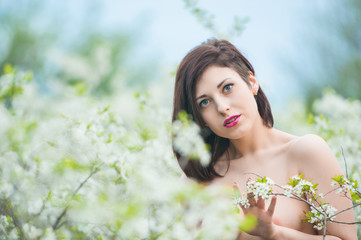 Fototapeta premium Closeup portrait of a young beautiful sexy brunette woman with white cherry flowers in bokeh background