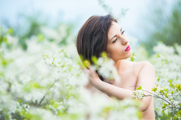 Closeup portrait of a young beautiful sexy brunette woman with white cherry flowers in bokeh background