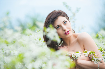 Closeup portrait of a young beautiful sexy brunette woman with white cherry flowers in bokeh background