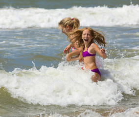 Happy blonde mother and daughter play among waves of sea