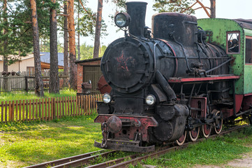 Fototapeta na wymiar Old black steam locomotive stands on rusty rails before fence. Talitsy, Yaroslavsky region, Russia.