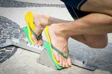 Brazilian athlete wearing flip flops crouching at the start position in running blocks on the tiles...