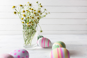 Bouquet of chamomiles in a glass vase and easter eggs in pastel