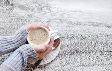 Female hands holding cups of coffee on wooden table background