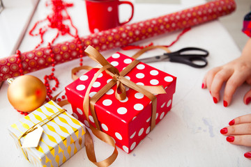 Female hands wrapping xmas gifts into paper and tying them up wi