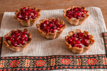 Five tartletes with custard and pomegranate on linen tablecloth.