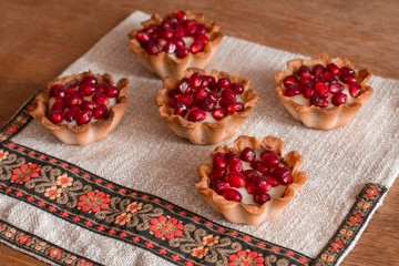 Five tartletes with custard and pomegranate on linen tablecloth.