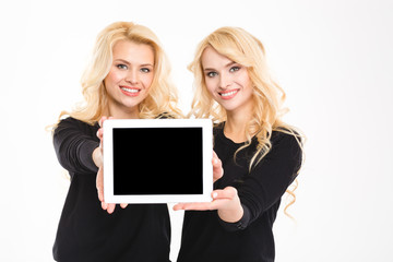 Naklejka premium Two cute lovely sisters twins showing blank tablet computer screen
