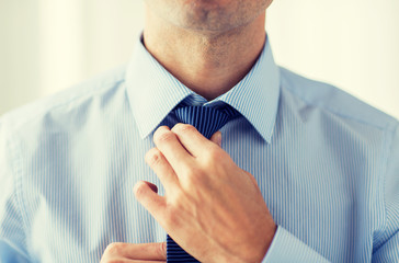 close up of man in shirt adjusting tie on neck