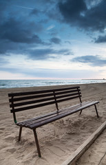 Empty wooden bench stands on sandy beach