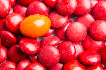 Concept of selective focus on orange chocolate candy against heaps of red candies at background