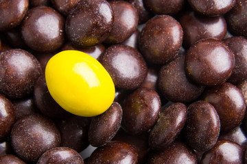 Concept of selective focus on yellow chocolate candy against heaps of brown candies at background