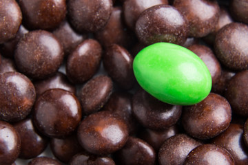 Concept of selective focus on green chocolate candy against heaps of brown candies at background