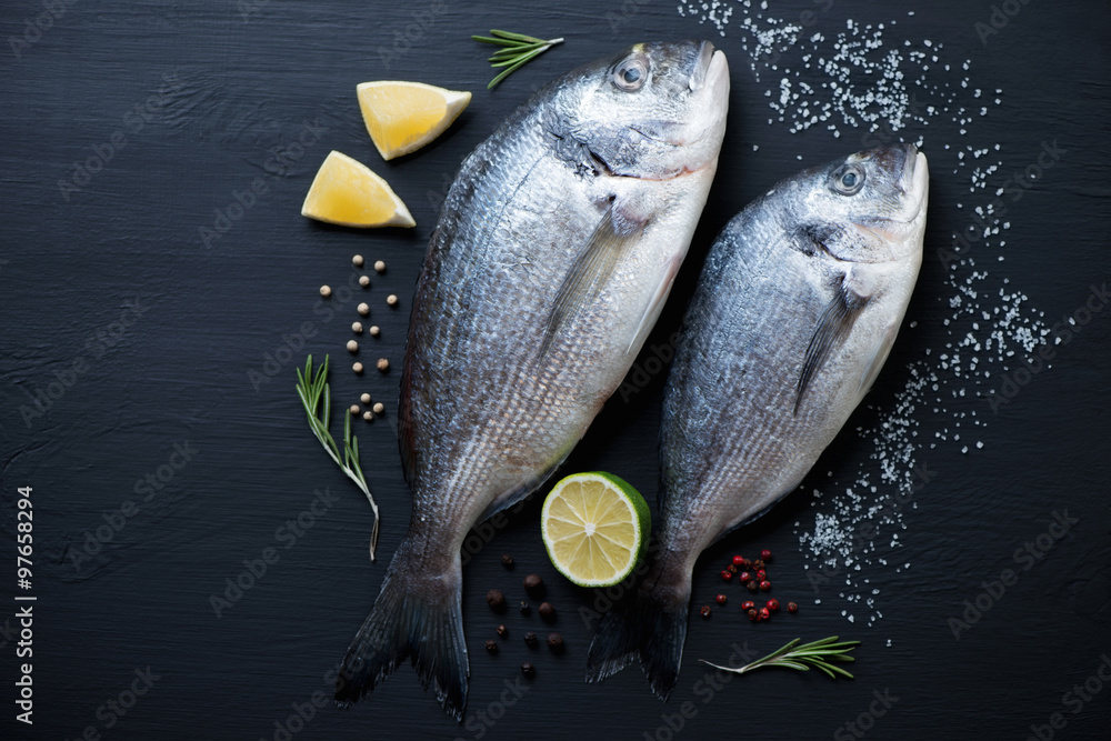 Wall mural top view of two uncooked dorada fishes on a black wooden surface