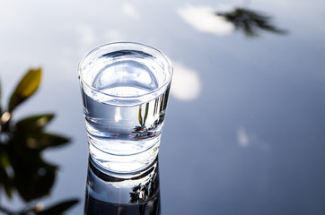 Refreshing purified water in transparent glass with reflection against blue sky, cloud and greeneries