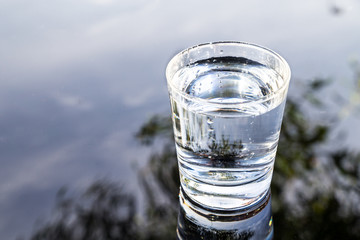 Refreshing purified water in transparent glass with reflection against blue sky, cloud and greeneries