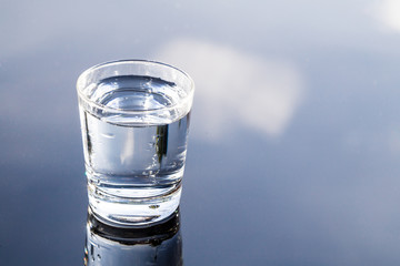 Refreshing purified water in transparent glass with reflection against blue sky and cloud