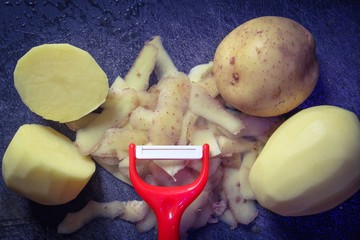 Potatoes and the peelings with a red potato peeler on a rustic chopping board