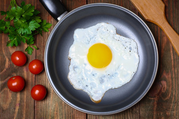 Pan of fried eggs, with cherry-tomatoes and parsley on a wooden table surface