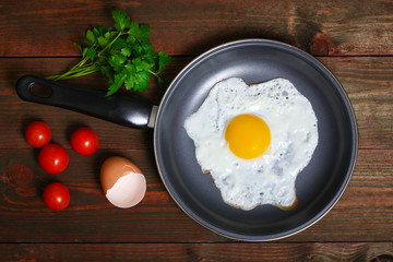 Pan of fried eggs, with cherry-tomatoes and parsley on a wooden table surface