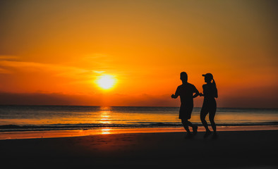 Fototapeta na wymiar Young couple: man and woman run together on a sunset on lake coa