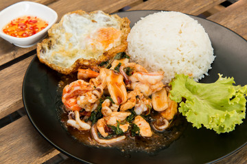 Rice topped with stir-fried combination of pork, chicken, squid, shrimp, basil and fried egg. Thai food.