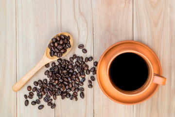 Coffee in ceramic cup and roasted coffee beans on wooden table. Top view. Pottery coffee cup. (Selective focus on cup)