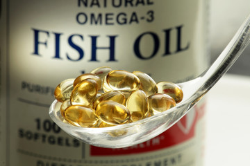 Fish oil softgels in a spoon, bottle with capsules on the background