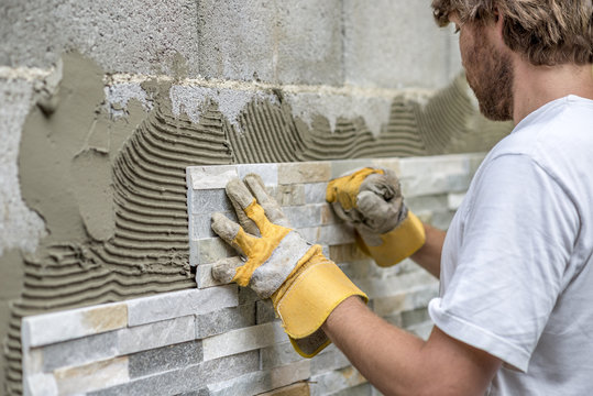 Man pressing an ornamental tile into a glue on a wall