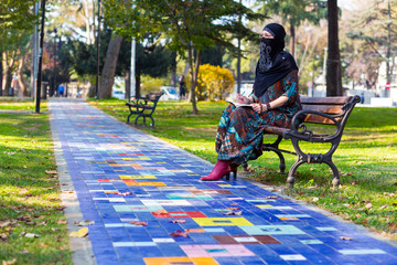 Young Islamic Woman sitting on bench in Park along colorful paved alley