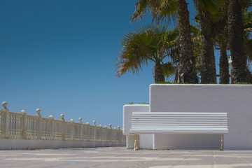 White bench against white wall and palm trees