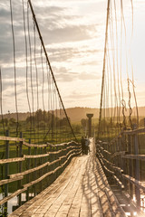 Old vanishing lengthy hanging wooden footbridge with rails over river and bright Sun in sky at sunset. Arkhangelsky region, Russia. 
