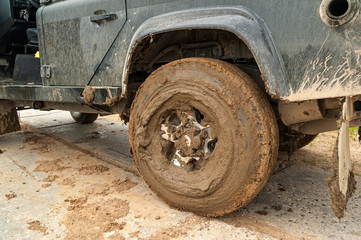 Off-road car fragment with muddy rear wheel on concrete pavement plate.
