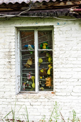 Window in white brick wall with numerous child's soft toys squeezed between glass and metal bars