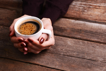 Female hands holding cup of coffee on wooden background