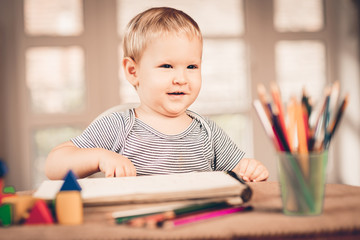 Blond boy laughing and crayons in front of him