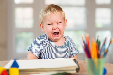 Little caucasian boy crying and crayons is in front