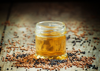 Oil of mustard in a small jar and yellow and black mustard seeds