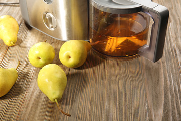 Stainless juice extractor with pears and glass of juice on wooden background, close up