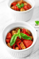 Tasty vegetarian ratatouille made of eggplants, squash, tomatoes in bowls on wooden table background