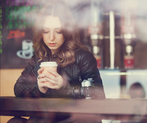 Young woman drinking coffee sitting indoor in urban cafe. Cafe city lifestyle. Casual portrait of teenager girl. Toned