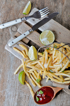 French fried potatoes in metal basket with sauce and lime on cutting board
