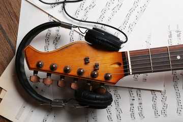 Electric guitar and headphones with music notes on wooden background, close-up