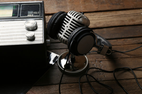 Microphone with headphones and radio on wooden background