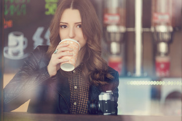 Young woman drinking coffee sitting indoor in urban cafe. Cafe city lifestyle. Casual portrait of teenager girl. Toned