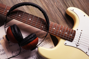 Electric guitar with headphones and musical notes on wooden background