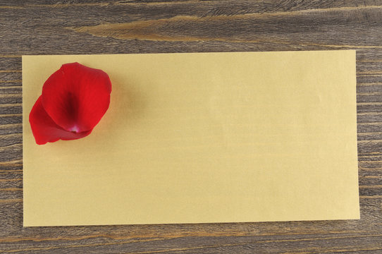 Red rose petals over paper envelope on a wooden background.