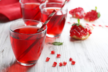 Three glasses of tasty juice and garnet fruit, on wooden background