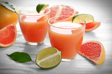 Two glasses of citrus juice and fresh fruits on light wooden background