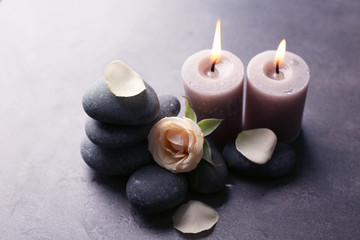 Obraz na płótnie Canvas Relax concept - composition of aroma candles with pebbles and flower on grey background